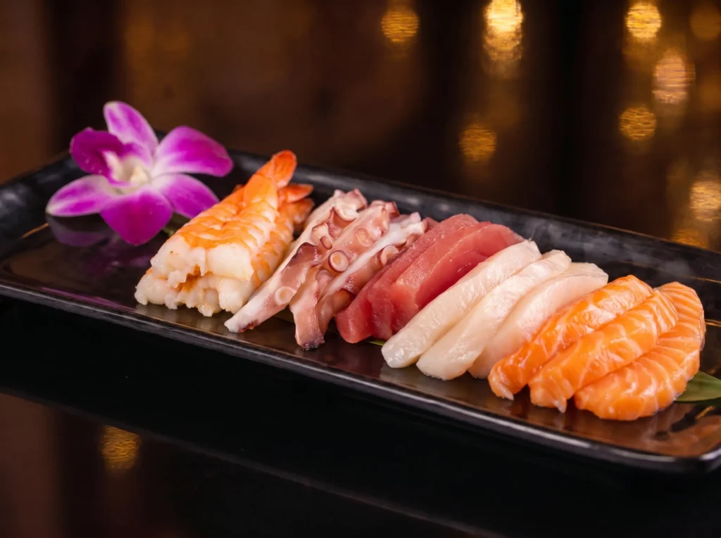Chef's Special Sashimi Mix at Kingdom Sushi, an assortment of salmon, tuna, white fish, octopus and shrimp on a black plate with an orchid and banana leaf