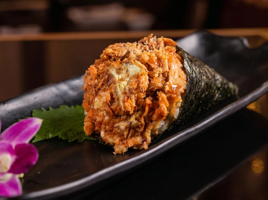 Grilled salmon temaki hand roll at Kingdom Sushi wrapped in crisp nori over rice, filled with flaked salmon and creamy sauce with a shiso leaf and orchid