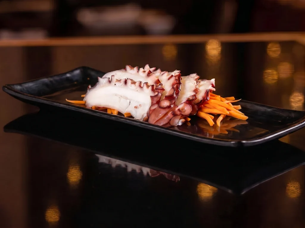 Octopus sashimi at Kingdom Sushi with tender sliced tako over shredded carrots on a black plate, showing purple suckers and white flesh
