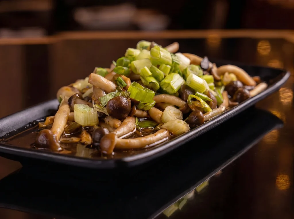 Sauteed shimeji mushrooms at Kingdom Sushi tossed in a savory brown sauce and topped with fresh chopped scallions on a black rectangular plate