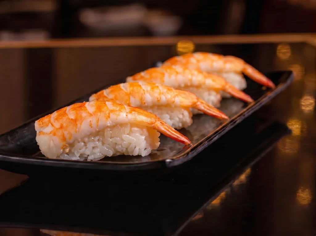 Shrimp Nigiri at Kingdom Sushi, four pieces of butterflied shrimp draped over pressed sushi rice and lined on a black plate