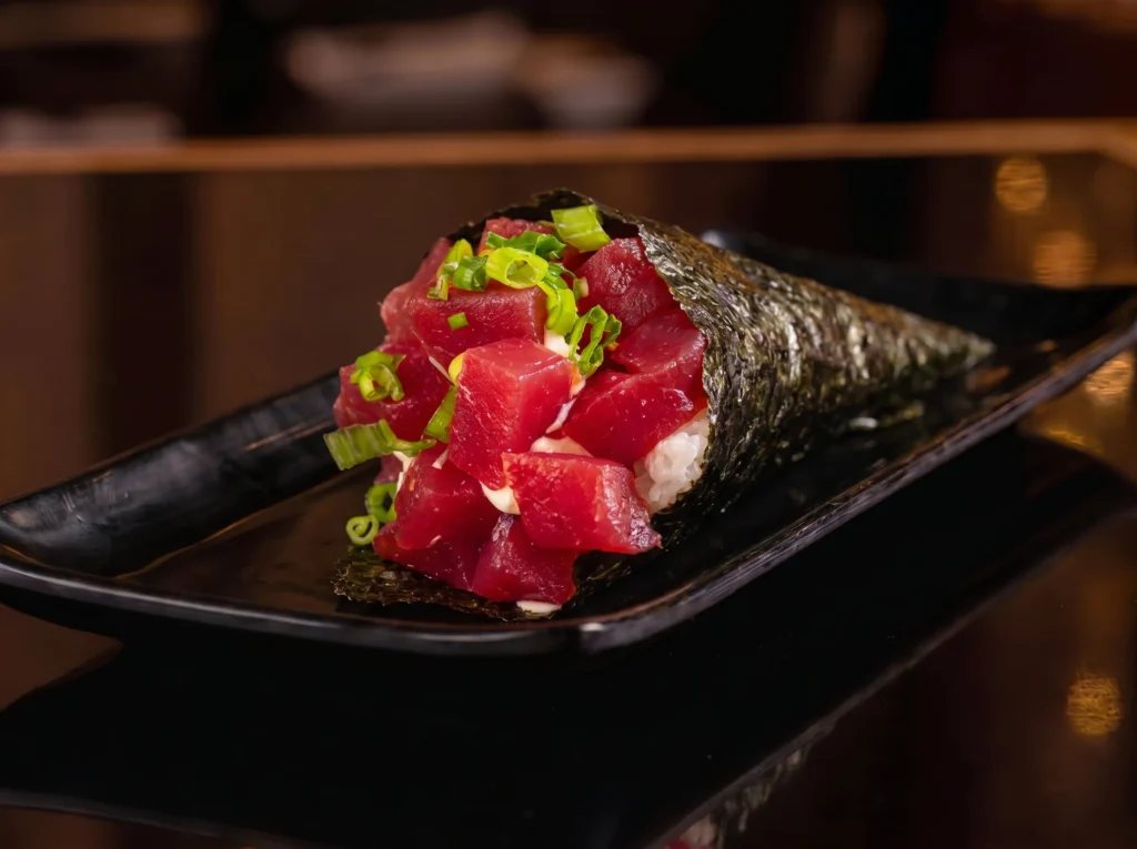 Tokyo Temaki hand roll at Kingdom Sushi filled with cubed raw tuna and scallions in a crisp nori cone on a black plate