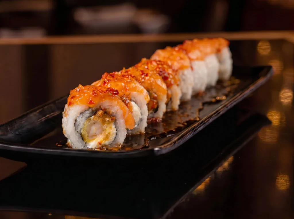 Uramaki Boss roll at Kingdom Sushi topped with salmon and sweet chili glaze, filled with tempura shrimp and cream cheese on a black plate