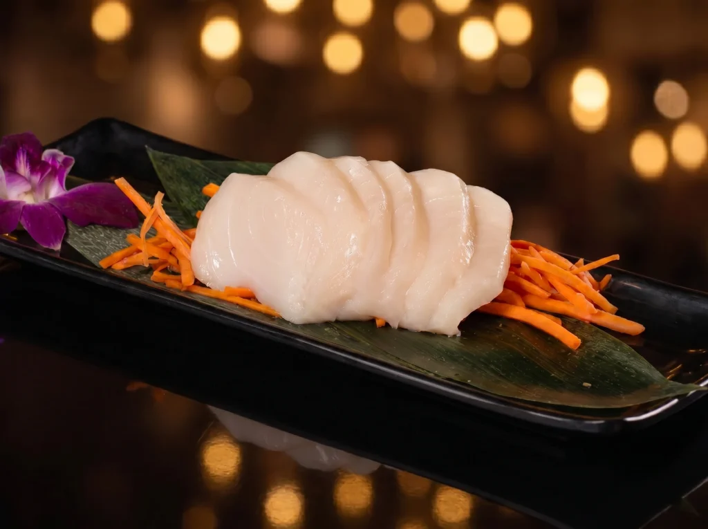 White fish sashimi at Kingdom Sushi, pearly translucent slices fanned over shredded carrots on a banana leaf with a purple orchid